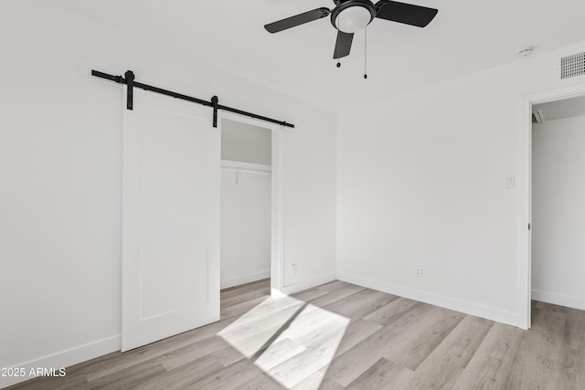 unfurnished bedroom with ceiling fan, light hardwood / wood-style floors, a closet, and a barn door