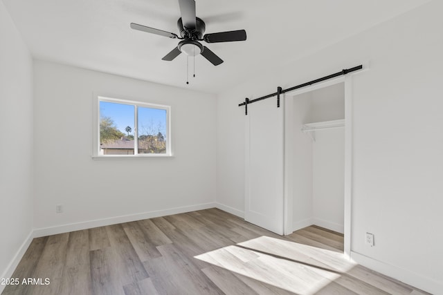 unfurnished bedroom with light wood-type flooring, ceiling fan, a barn door, and a closet