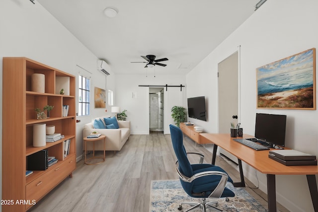 home office featuring a wall mounted AC, ceiling fan, a barn door, and light hardwood / wood-style flooring