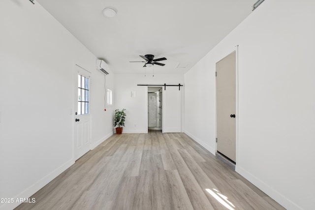 spare room featuring ceiling fan, a wall unit AC, a barn door, and light hardwood / wood-style floors