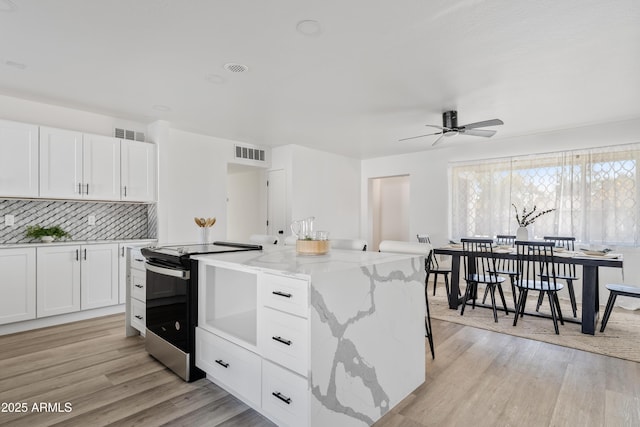 kitchen with electric range, light stone countertops, ceiling fan, white cabinets, and tasteful backsplash