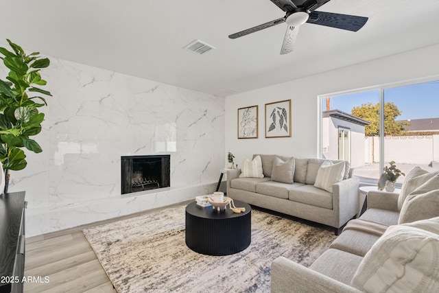 living room with a fireplace, light wood-type flooring, and ceiling fan