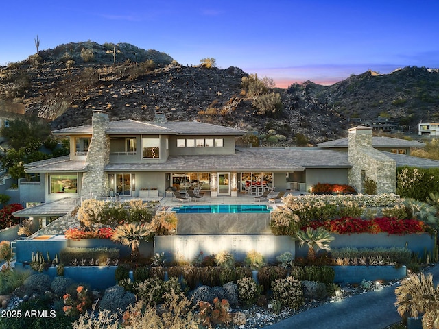 back house at dusk with a mountain view and a patio