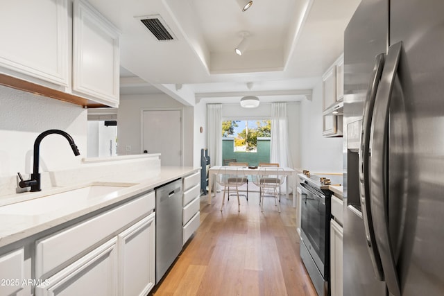 kitchen featuring light stone counters, stainless steel appliances, a tray ceiling, white cabinets, and sink