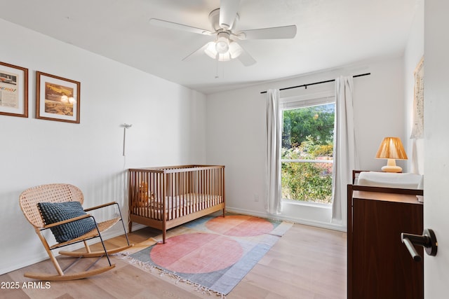 bedroom with a nursery area, light wood-type flooring, and ceiling fan