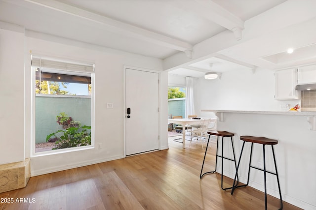 kitchen with white cabinets, beamed ceiling, light wood-type flooring, a breakfast bar area, and backsplash