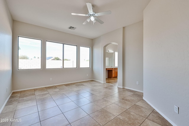 spare room featuring arched walkways, ceiling fan, light tile patterned floors, visible vents, and baseboards