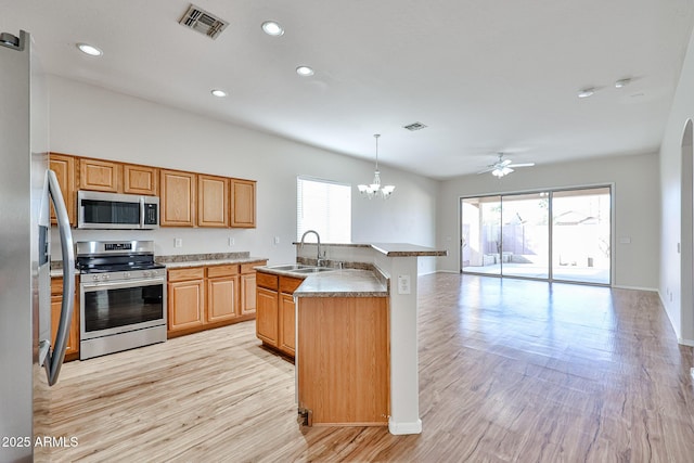 kitchen featuring stainless steel appliances, a sink, open floor plan, light countertops, and decorative light fixtures