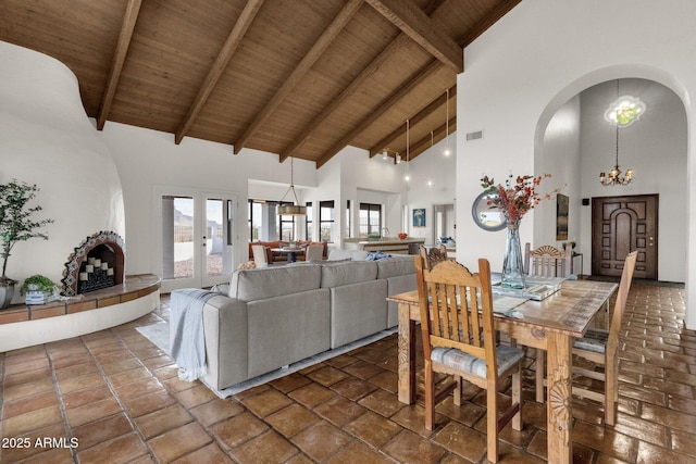 dining area featuring a tile fireplace, high vaulted ceiling, beamed ceiling, wood ceiling, and a chandelier