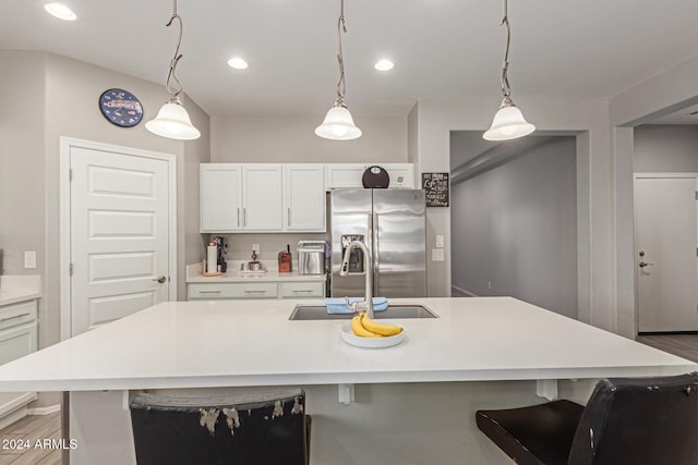 kitchen featuring stainless steel fridge, a kitchen island with sink, sink, hardwood / wood-style floors, and white cabinetry