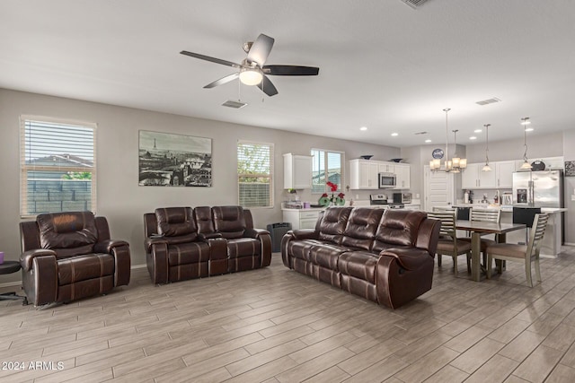 living room featuring ceiling fan with notable chandelier and light wood-type flooring