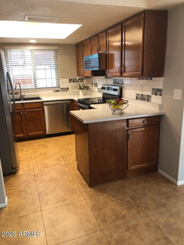 kitchen with tasteful backsplash, light countertops, appliances with stainless steel finishes, a sink, and a peninsula