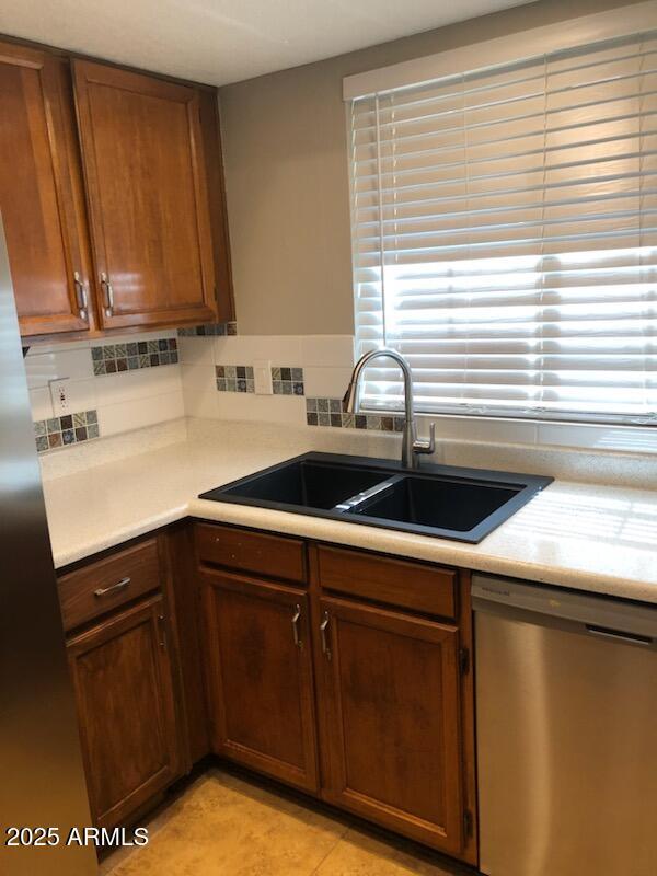 kitchen featuring light tile patterned floors, decorative backsplash, light countertops, stainless steel dishwasher, and a sink