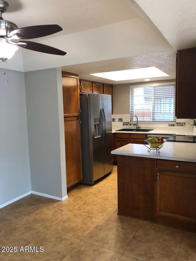 kitchen featuring baseboards, stainless steel fridge with ice dispenser, a peninsula, light countertops, and a sink