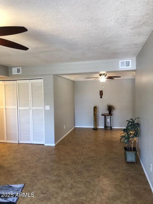 spare room with ceiling fan, a textured ceiling, visible vents, and baseboards