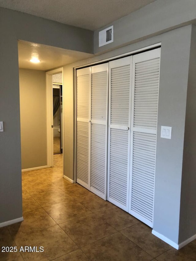 hallway featuring baseboards, a textured ceiling, visible vents, and tile patterned flooring