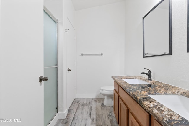 full bath with double vanity, a stall shower, toilet, wood finished floors, and a sink