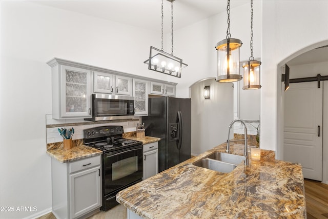 kitchen with a barn door, arched walkways, decorative backsplash, black appliances, and a sink