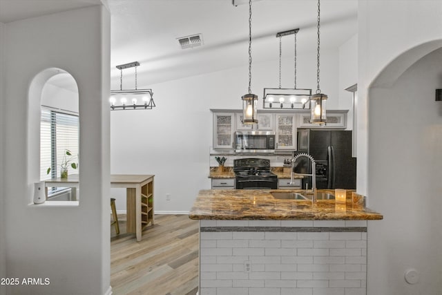 kitchen featuring light wood-style flooring, a sink, visible vents, backsplash, and black appliances