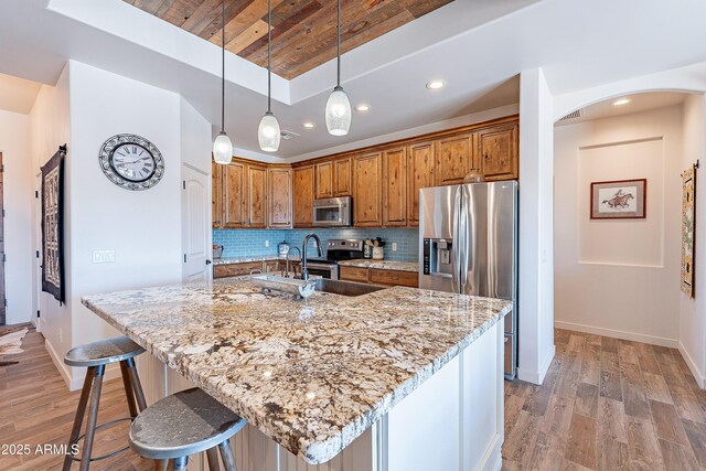 kitchen featuring arched walkways, backsplash, appliances with stainless steel finishes, light wood-style floors, and light stone countertops