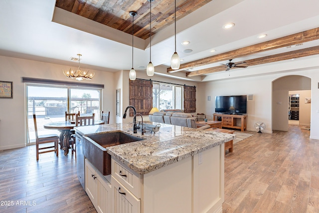 kitchen with arched walkways, light wood-style flooring, a sink, a raised ceiling, and pendant lighting