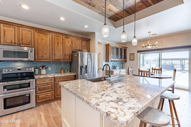 kitchen featuring visible vents, appliances with stainless steel finishes, brown cabinets, a breakfast bar area, and light wood-type flooring