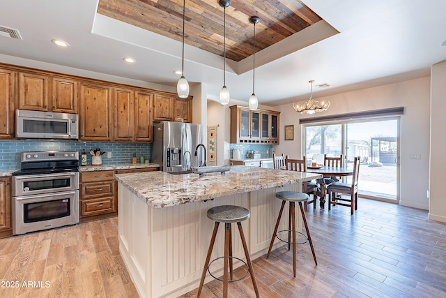 kitchen featuring light stone counters, appliances with stainless steel finishes, brown cabinets, tasteful backsplash, and a raised ceiling