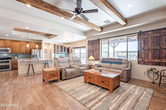 living area with a barn door, visible vents, a raised ceiling, and light wood-style flooring