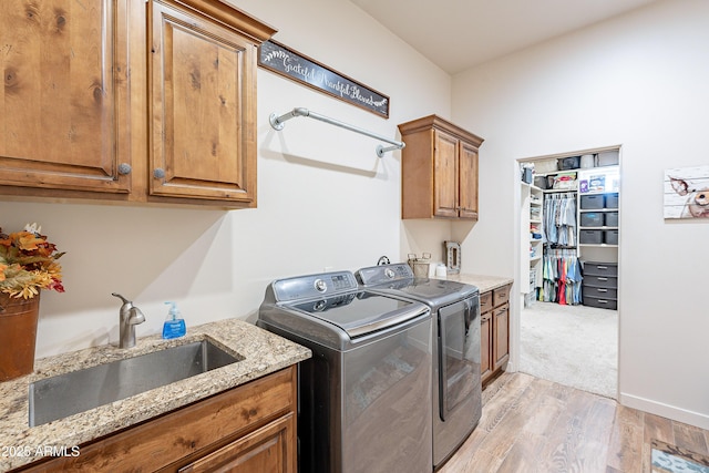 laundry area with cabinet space, light wood-style floors, a sink, washer and dryer, and baseboards