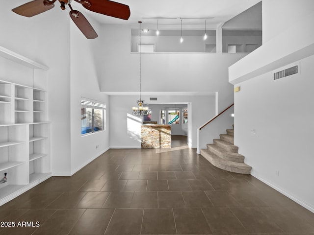 unfurnished living room with track lighting, a towering ceiling, ceiling fan with notable chandelier, and dark tile patterned floors