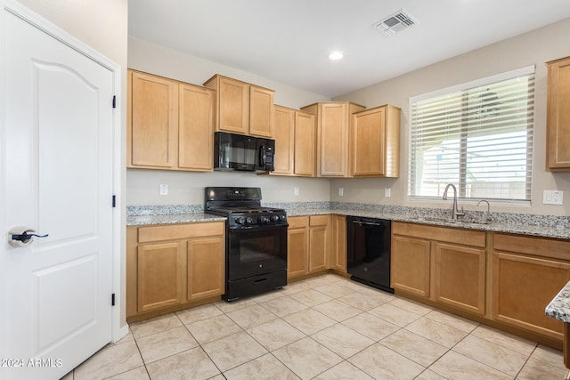 kitchen with light stone counters, black appliances, sink, and light tile patterned floors