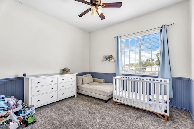 carpeted bedroom featuring a nursery area and ceiling fan