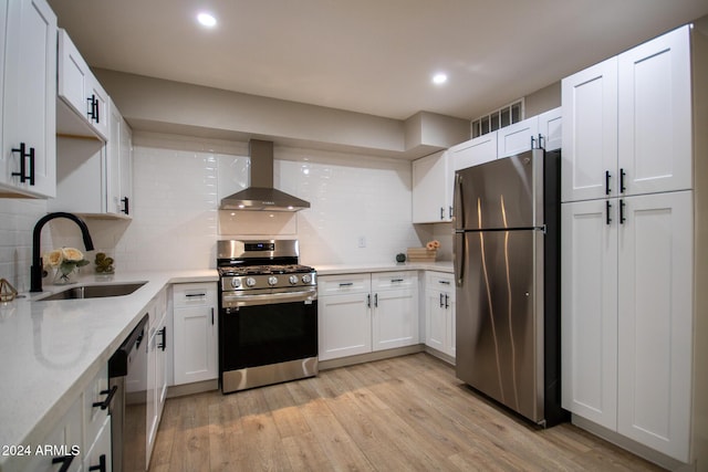 kitchen with white cabinetry, sink, stainless steel appliances, and wall chimney range hood