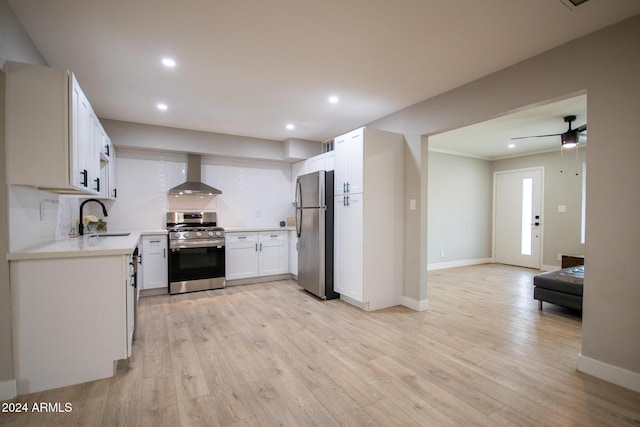 kitchen with appliances with stainless steel finishes, light hardwood / wood-style floors, white cabinetry, and wall chimney exhaust hood