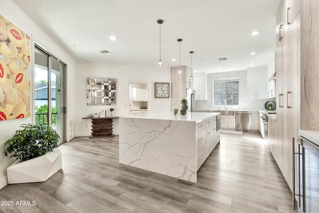 kitchen with a center island, pendant lighting, high end appliances, visible vents, and white cabinetry