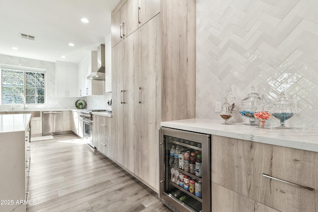 kitchen with wine cooler, stainless steel appliances, visible vents, wall chimney range hood, and modern cabinets