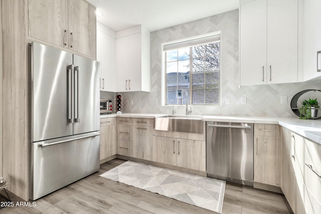 kitchen with stainless steel appliances, light countertops, light wood-style floors, light brown cabinets, and a sink