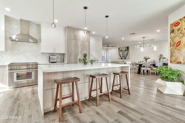 kitchen featuring wall chimney exhaust hood, modern cabinets, a breakfast bar, decorative light fixtures, and high end stainless steel range