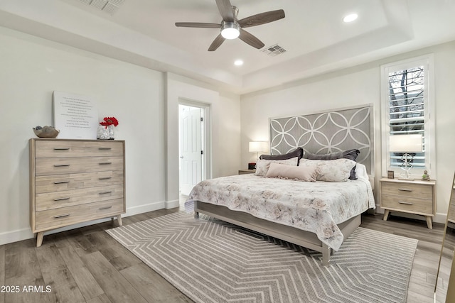 bedroom featuring a tray ceiling, visible vents, dark wood finished floors, and baseboards