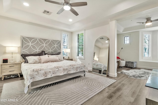 bedroom featuring a tray ceiling, multiple windows, wood finished floors, and visible vents