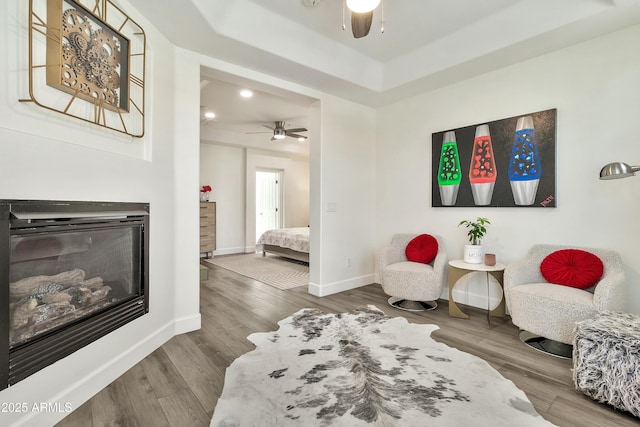 sitting room featuring a ceiling fan, baseboards, wood finished floors, and a glass covered fireplace