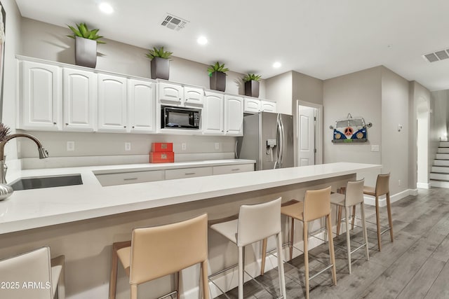 kitchen with light countertops, white cabinetry, a sink, black microwave, and stainless steel fridge with ice dispenser