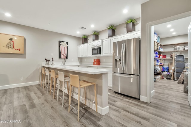 kitchen featuring black microwave, a breakfast bar area, white cabinets, light countertops, and stainless steel fridge with ice dispenser