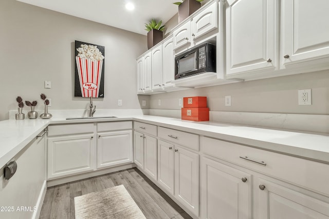 kitchen with black microwave, light countertops, a sink, and white cabinets