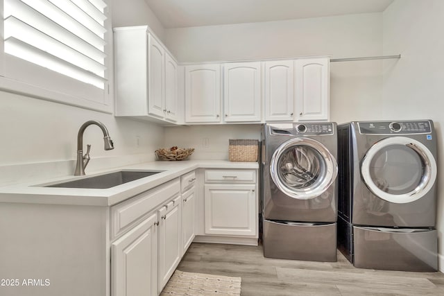 clothes washing area with light wood-type flooring, independent washer and dryer, a sink, and cabinet space