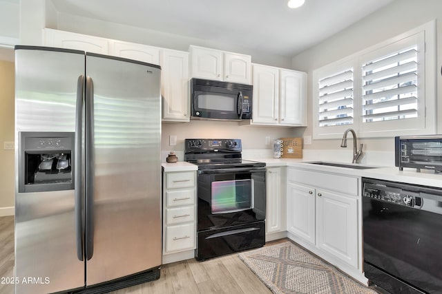 kitchen featuring light wood-style flooring, a sink, white cabinets, light countertops, and black appliances