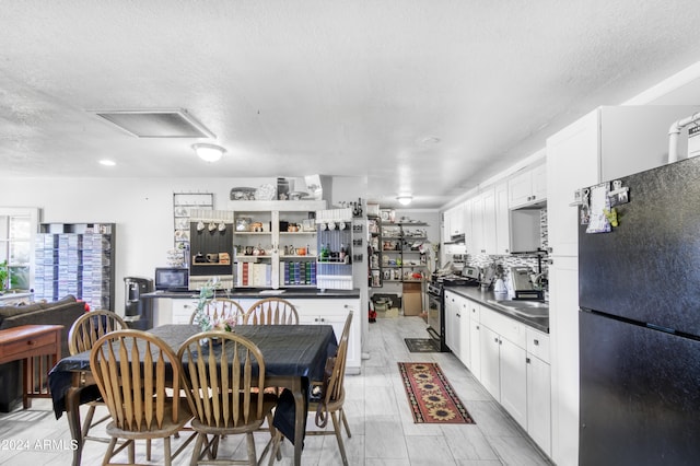 kitchen with black fridge, stainless steel range, white cabinetry, and a textured ceiling