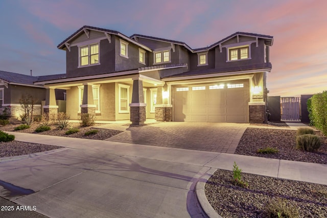 craftsman house featuring an attached garage, covered porch, a gate, decorative driveway, and stucco siding