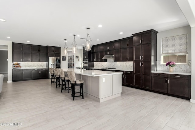 kitchen with stainless steel appliances, light countertops, hanging light fixtures, backsplash, and under cabinet range hood