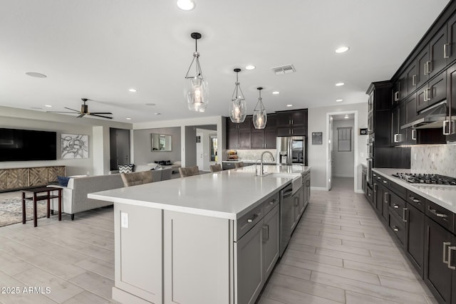 kitchen with under cabinet range hood, stainless steel appliances, a sink, visible vents, and decorative backsplash